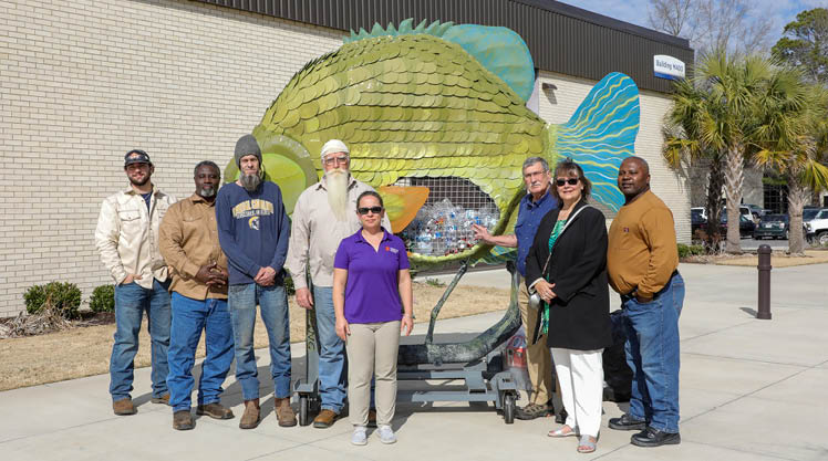 Welded fish litter sculpture with the group of individuals that participated in the creation of it.